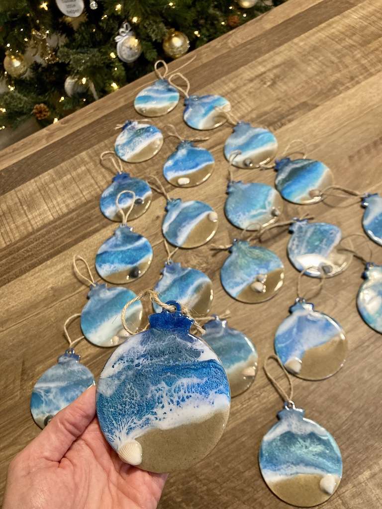 Multiple wooden round Christmas tree ornaments with resin in coastal design.