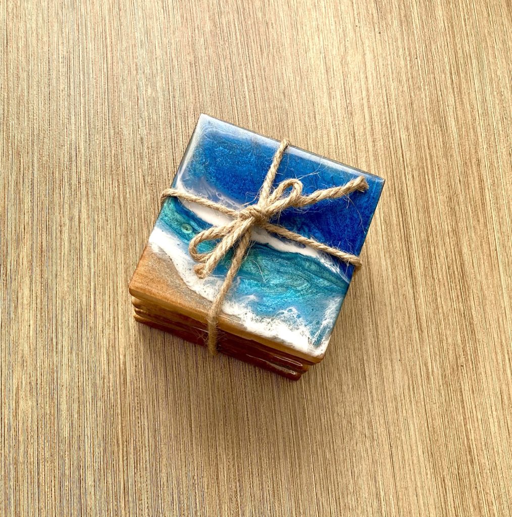 Set of four square wooden coasters decorated with resin for coastal waves and sand.