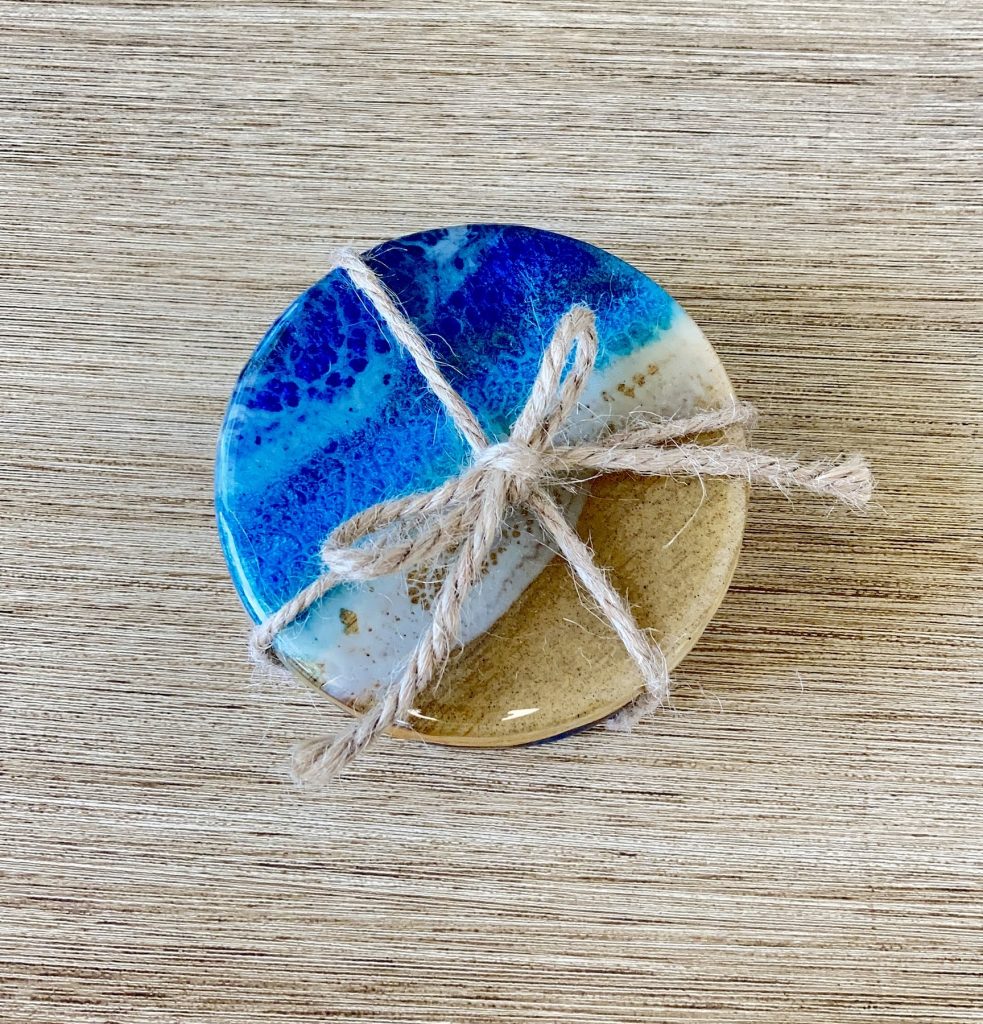 Set of four round wooden coasters decorated with resin for coastal waves and sand.