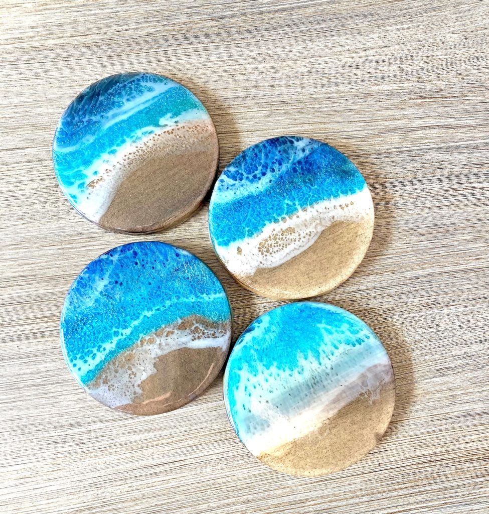 Set of four round wooden coasters decorated with resin for coastal waves and sand.