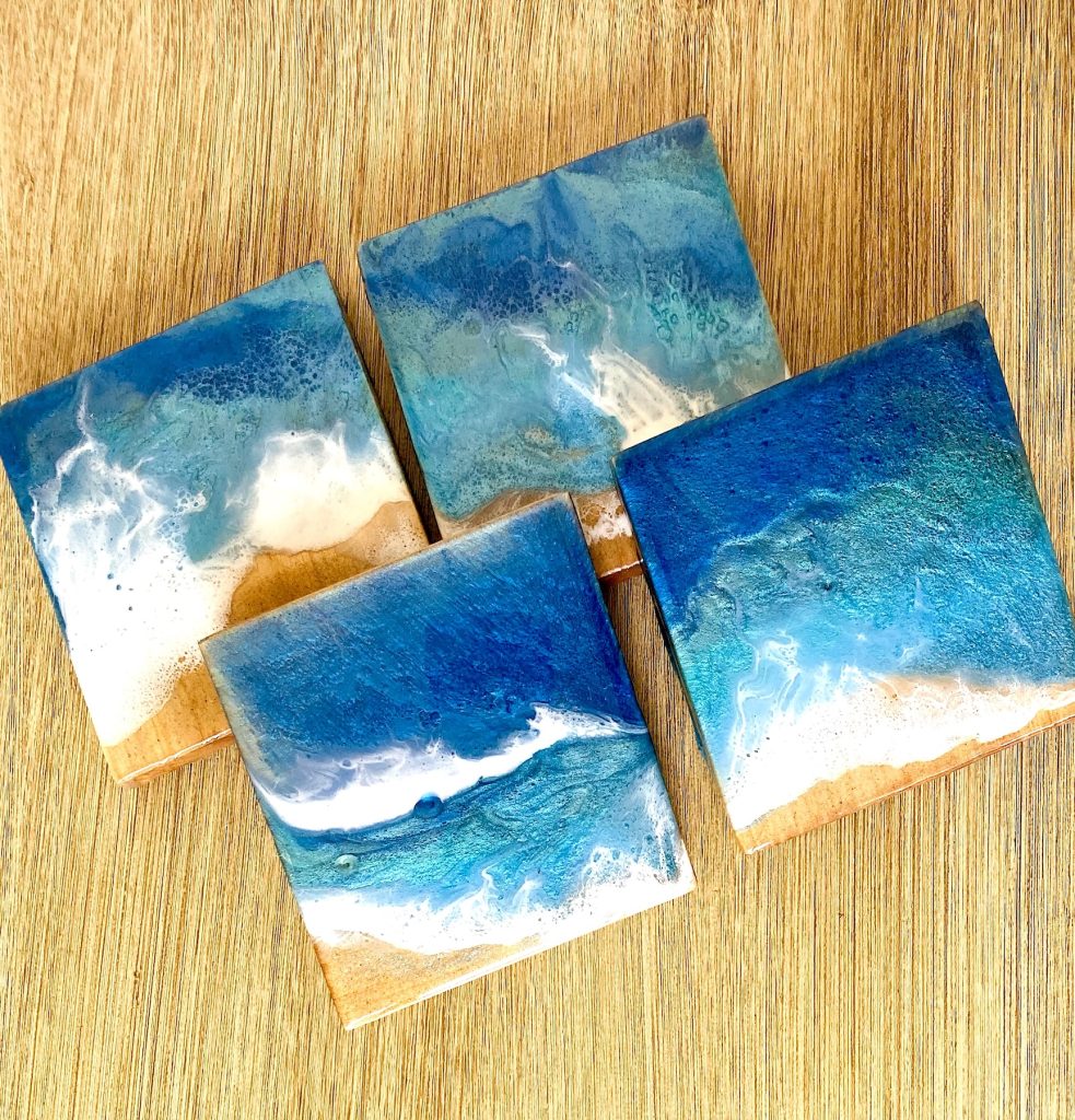 Set of four square wooden coasters decorated with resin for coastal waves and sand.