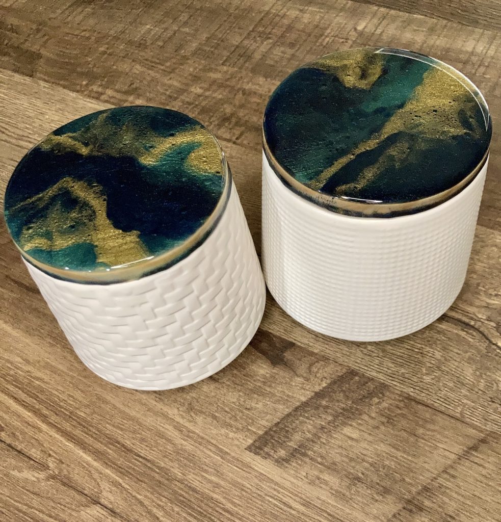 Set of two ceramic canisters. One with a waffle design and the other with a basket weave design. Wooden lids are covered with hand-poured epoxy resin in hues of dark blues and greens with ribbons of gold.